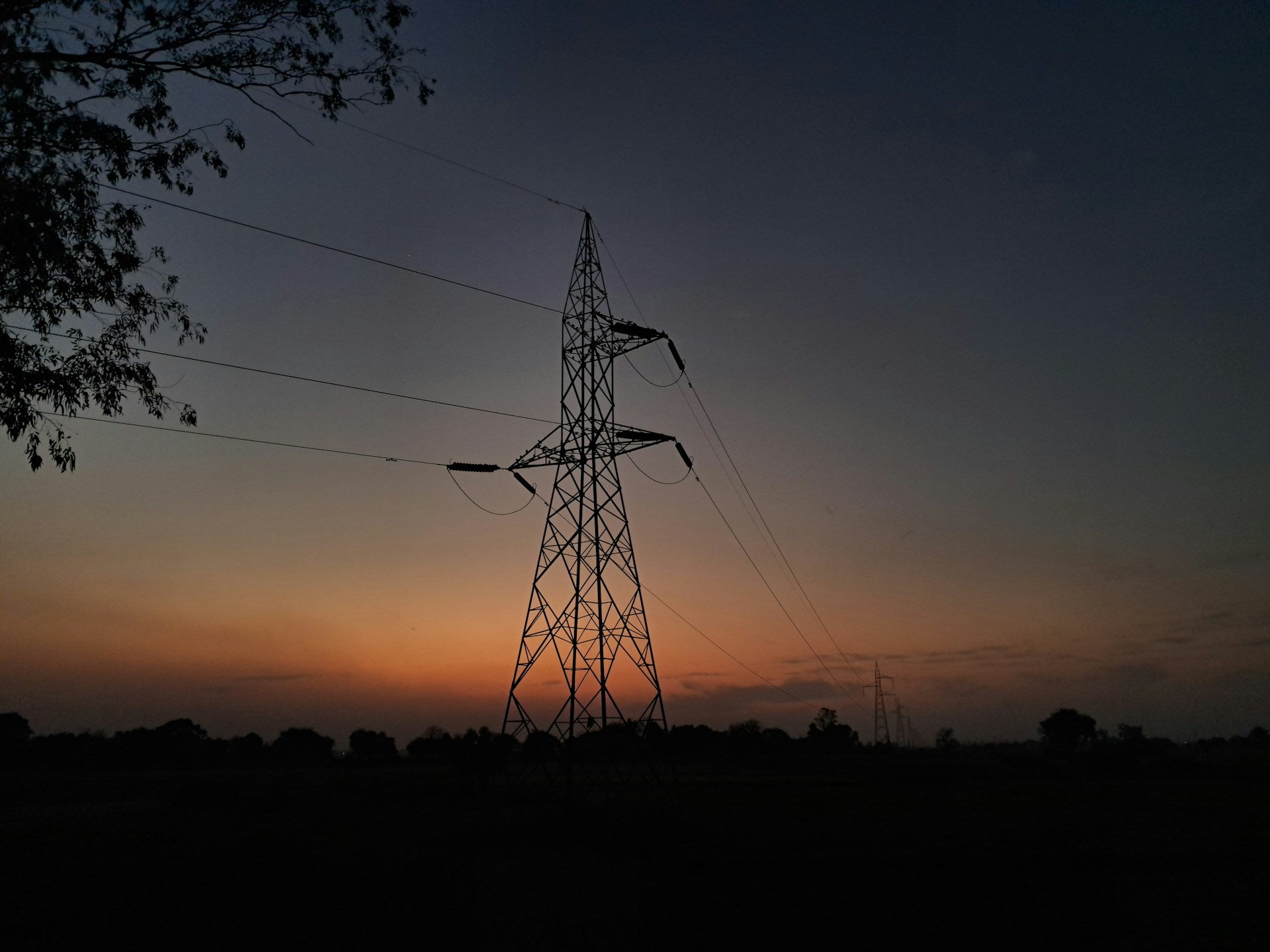 Electric power tower silhouette against a sunset sky